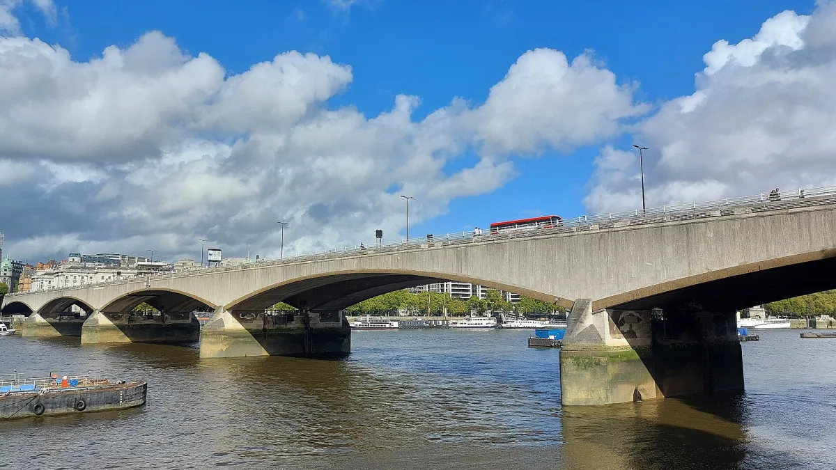 Waterloo Bridge in London, its concrete arches seen from the south bank of the Thames, with a red bus crossing.