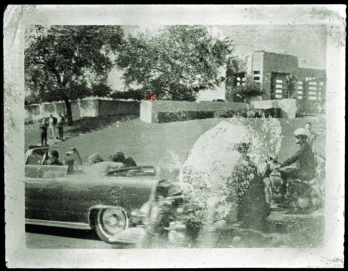 A car accompanied by two bikers, inside President Kennedy and his wife Jacqueline reacting to gunshots.