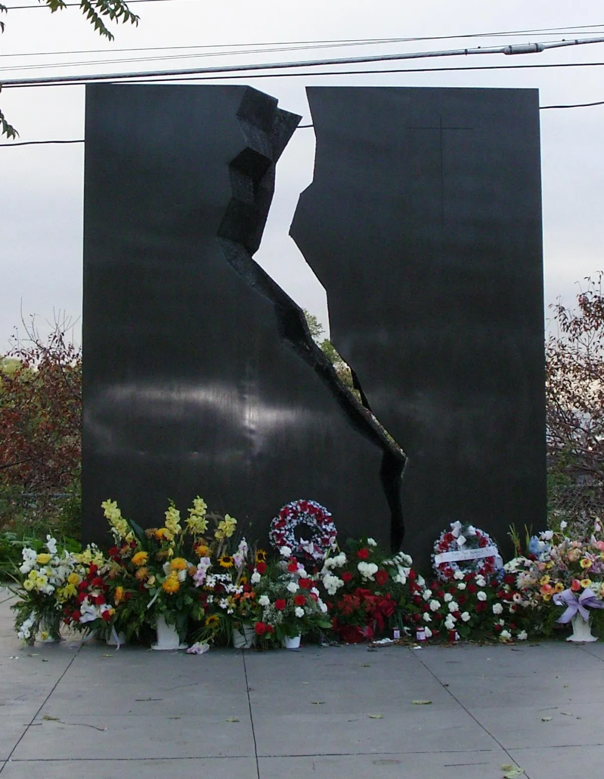 The Katyn memorial in Toronto: a tall black monolith split by a jagged vertical cleft, with wreaths and flowers banked along its base.