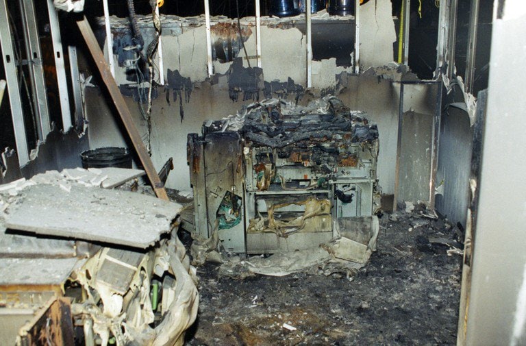 Interior office space gutted by fire, with collapsed ceiling and burned equipment.