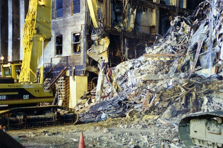 Excavators clearing structural debris piled against the damaged wall.
