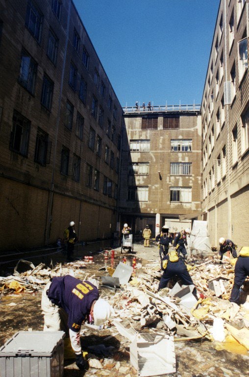 Recovery workers sifting a debris field in a courtyard between wings.