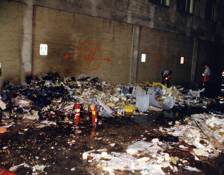 A debris field banked against the exterior wall at night, search markings on the wall above.
